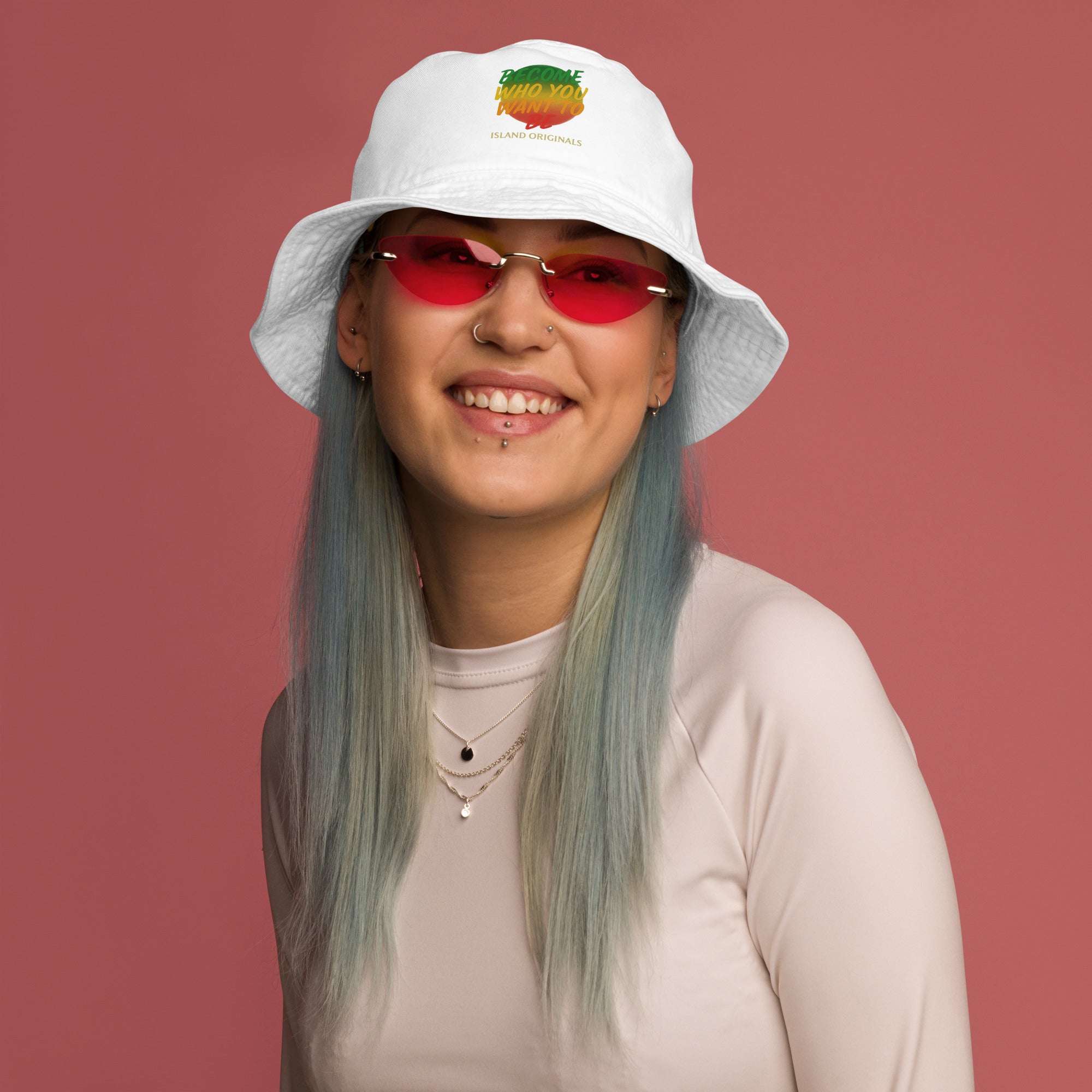 Person wearing a white bucket hat with a colorful design and red sunglasses on a pink background
