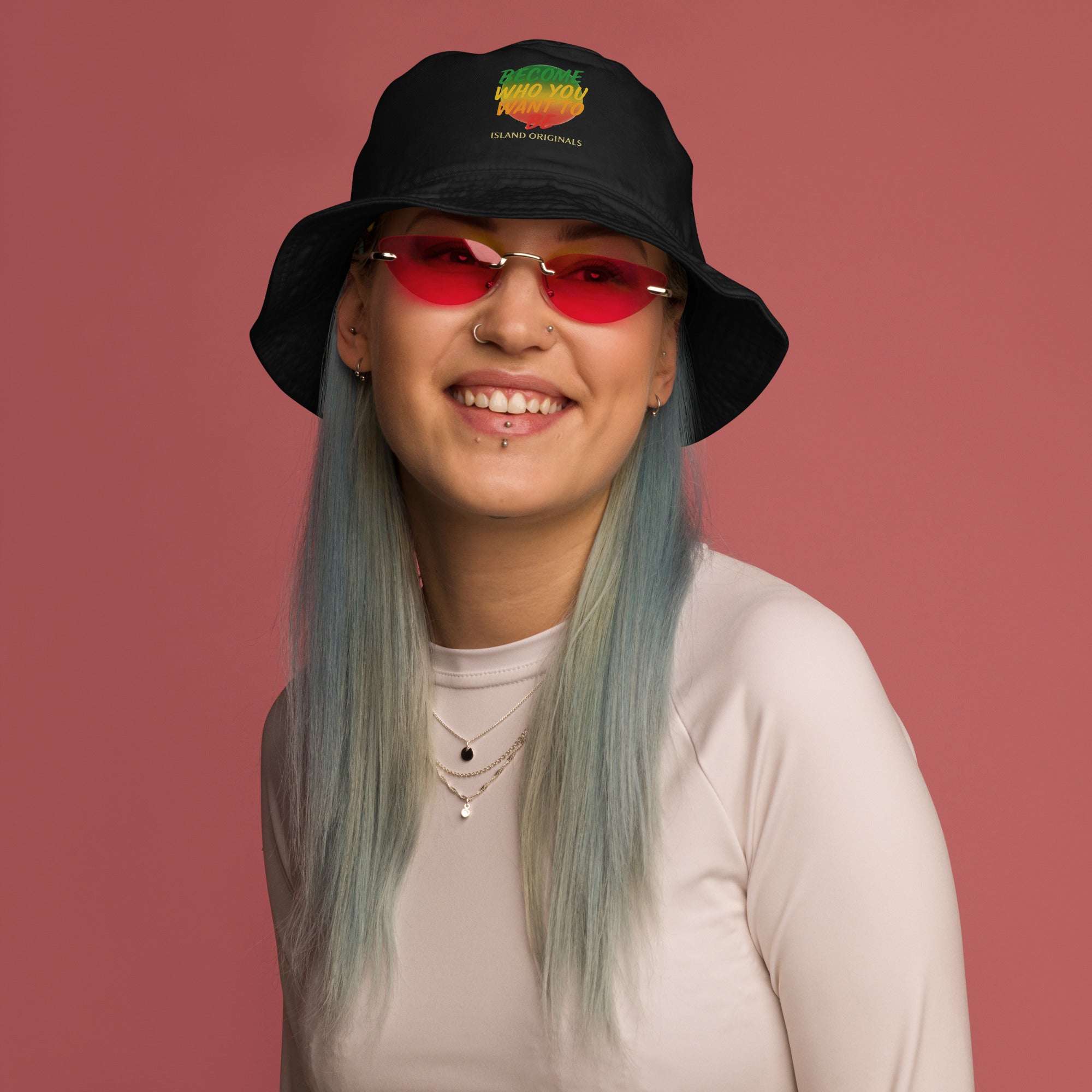 Person wearing a black bucket hat with colorful design and red sunglasses against a pink background