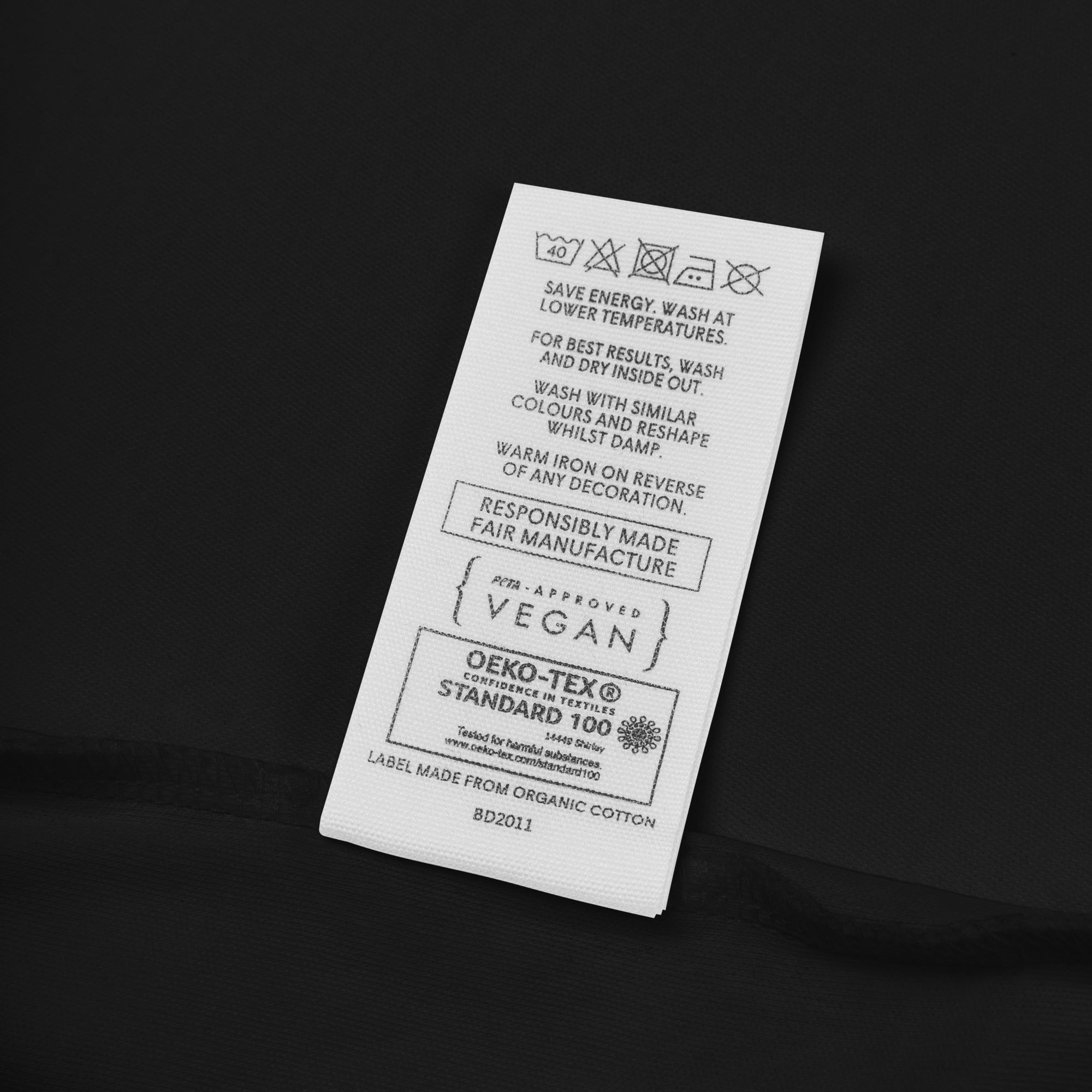 Textile label with care instructions and certification details on a black background
