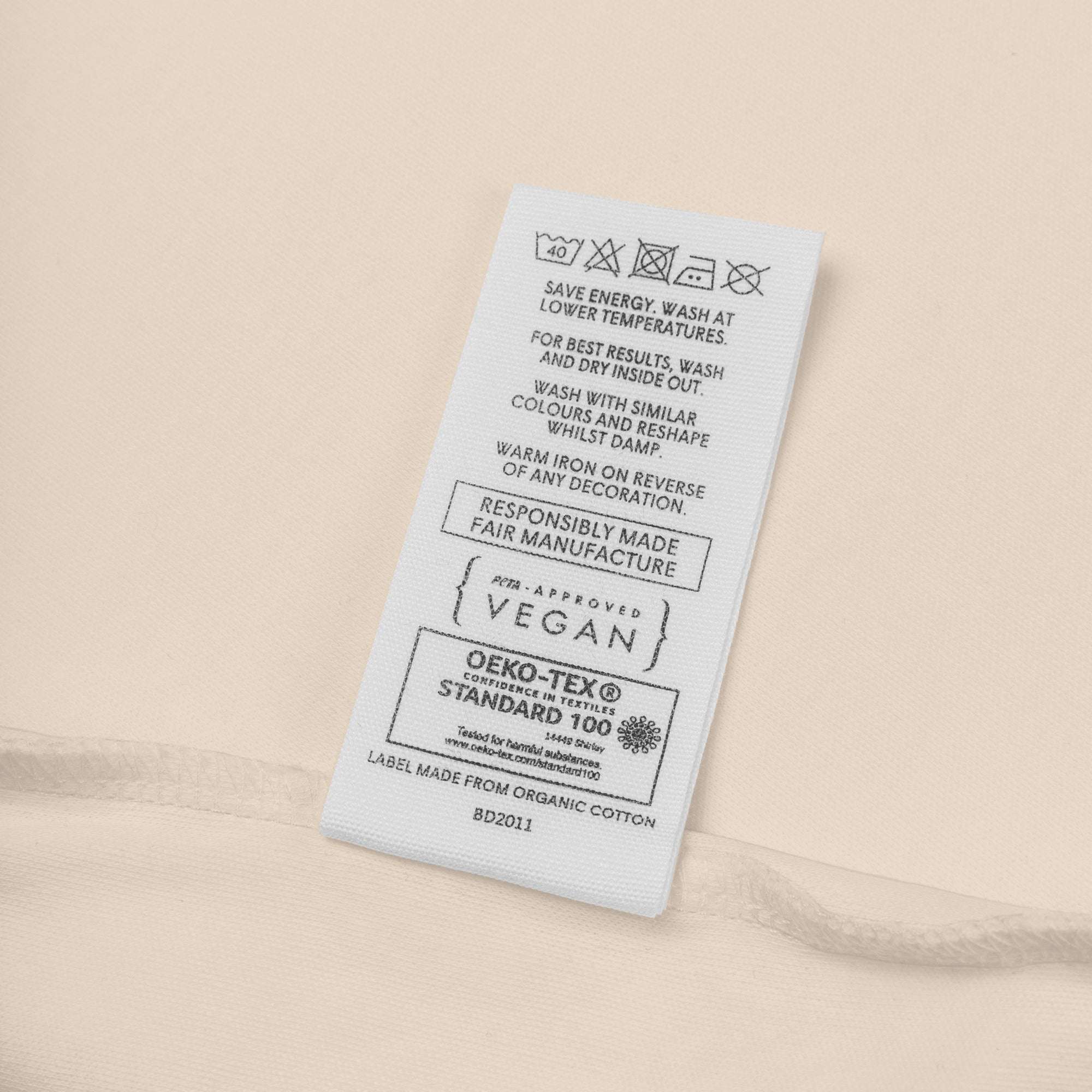 Fabric tag with care instructions and certification logos on a beige background