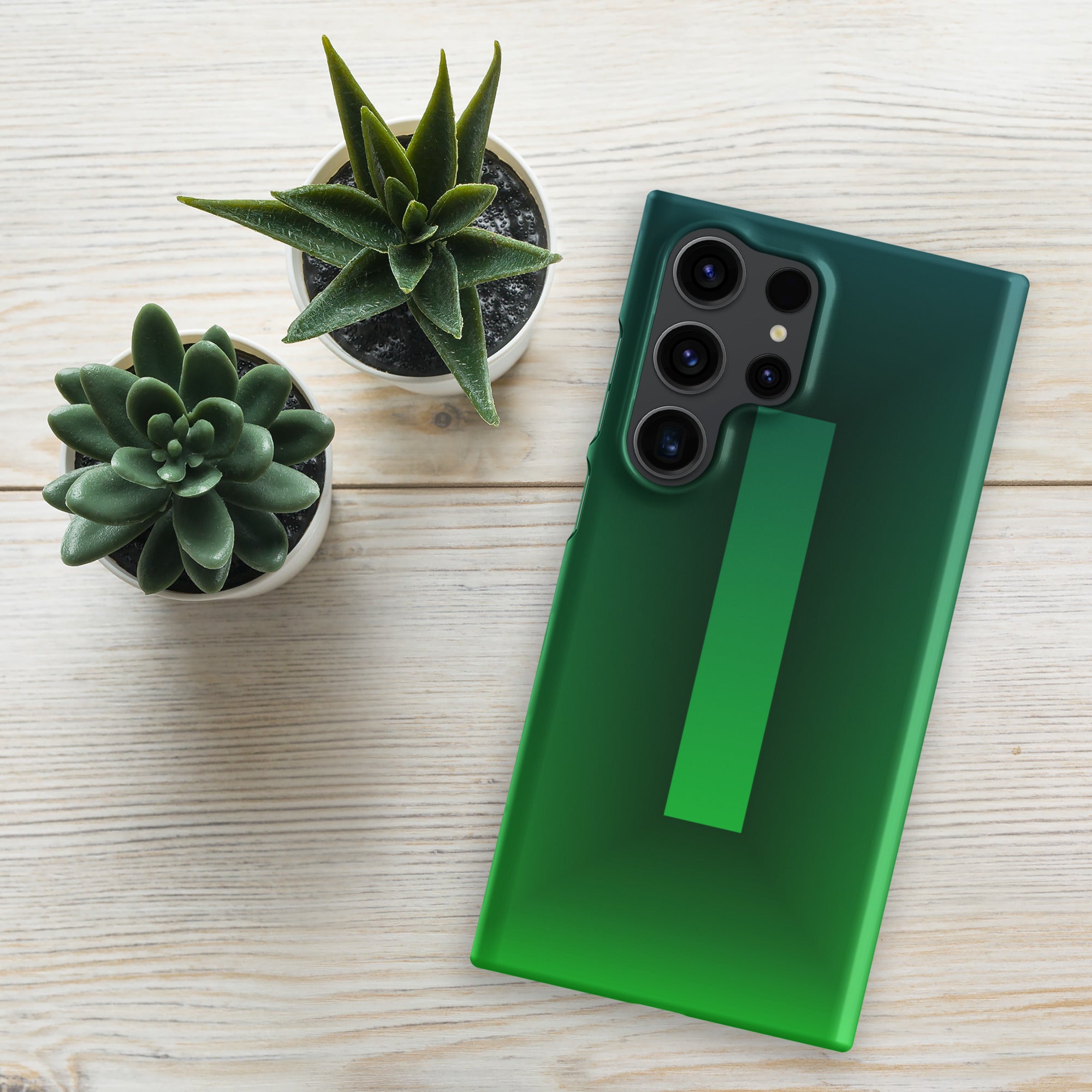 Green phone case on a smartphone with two small potted plants on a light wooden surface