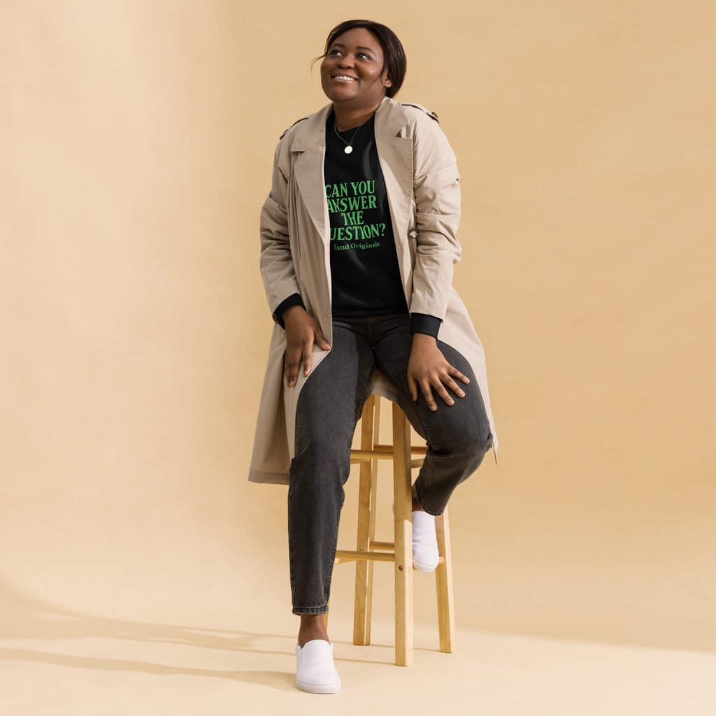 Woman sitting on a stool wearing a trench coat and black shirt with text, against a beige background